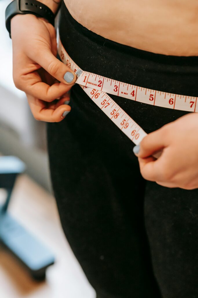 pexels-photo-6551070-6551070 From above of crop anonymous plump female using measuring tape around hips in gym